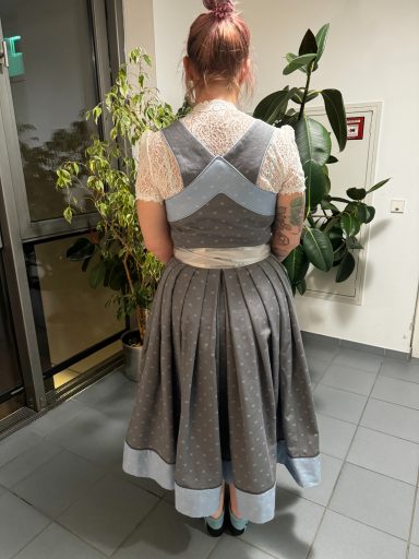 Dame mit rotem Haarknoten trägt ein graues Dirndl mit blauen Akzenten.