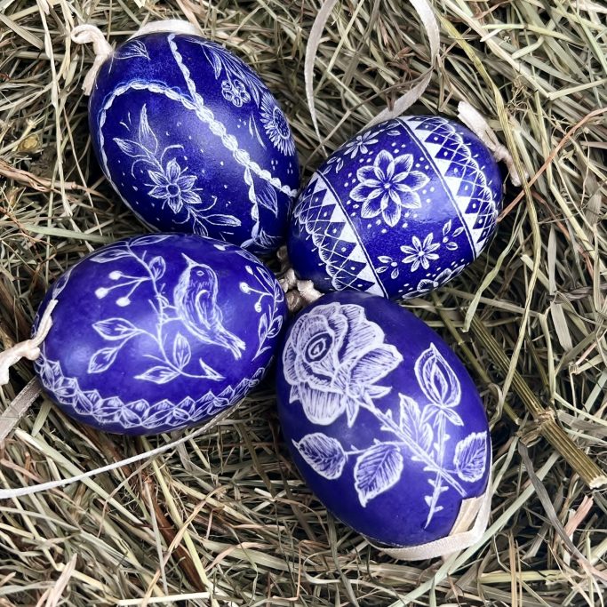 Blaue Ostereier mit filigranen weißen Mustern auf Heu arrangiert.
