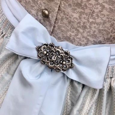 Blaue Schürzenschleife mit einer großen, verzierten Brosche in der Mitte.