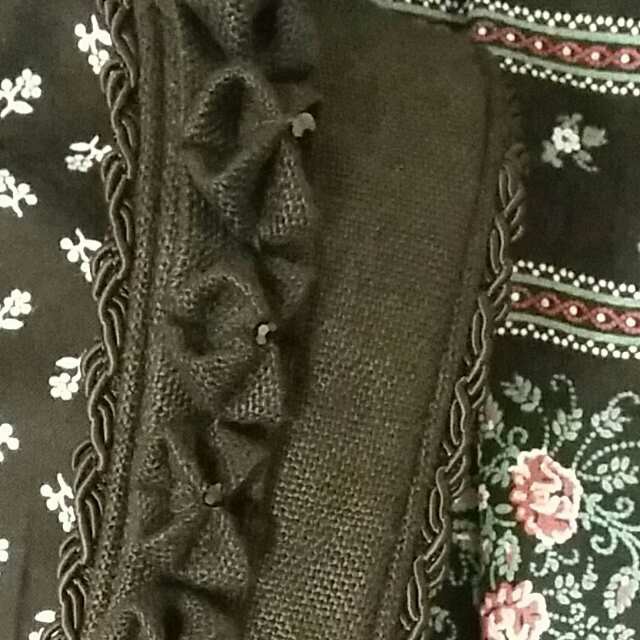 Detailansicht eines schwarzen Stoffes mit Rüschendekor und floralem Muster.