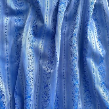 Zarte blaue Drapierung mit floralen Mustern auf einem hellen Hintergrund.