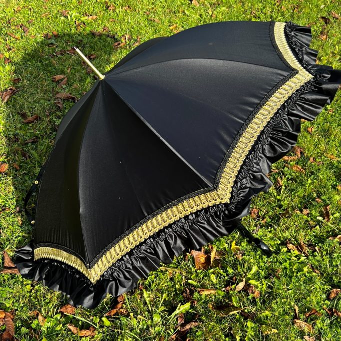 Schwarzer Regenschirm mit Rüschenrand auf grünem Gras.