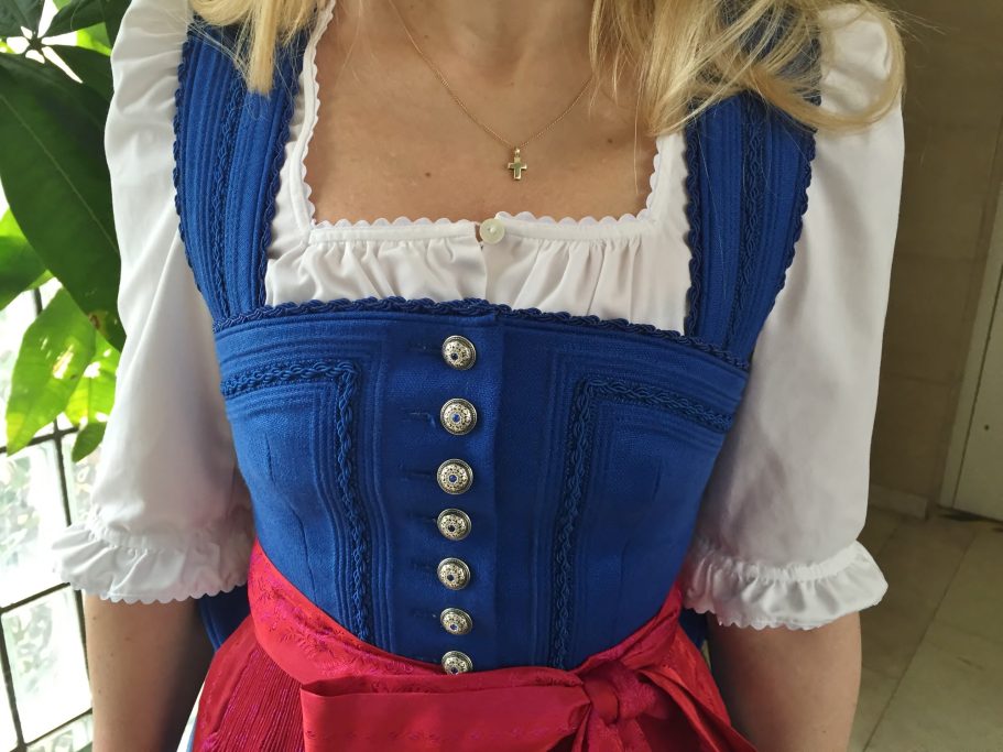 Traditionelles bayerisches Dirndl in Blau mit roten Akzenten und weißen Blusenärmeln.