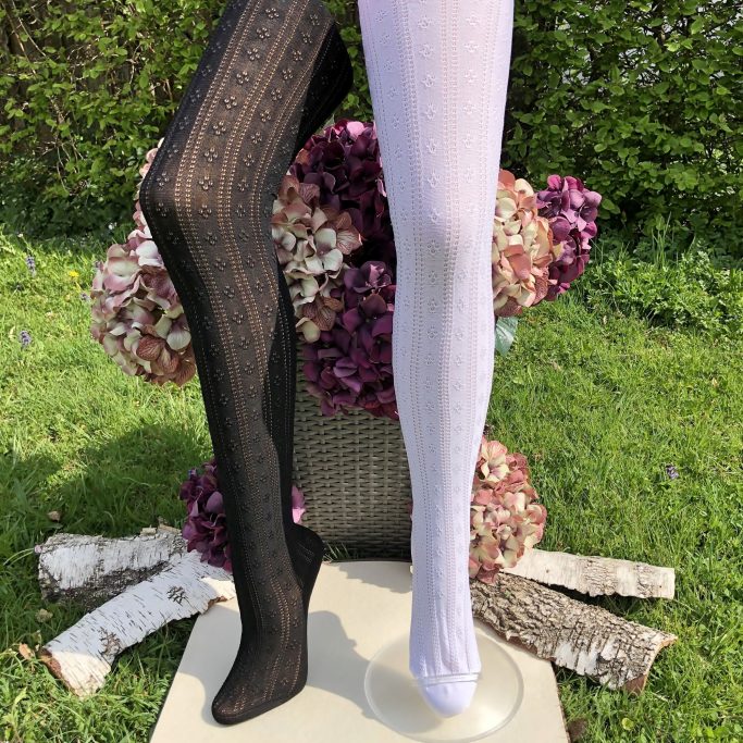 Schwarze und weiße Strumpfhosen mit Muster, präsentiert auf einem Ständer vor Blumen.