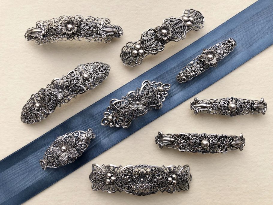 Schmuckstücke aus Silber mit Perlen und zarten floralen Mustern auf blauer Unterlage.