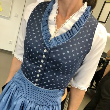 Frau trägt ein traditionelles bayerisches Dirndl in Blau mit Rüschendetails.