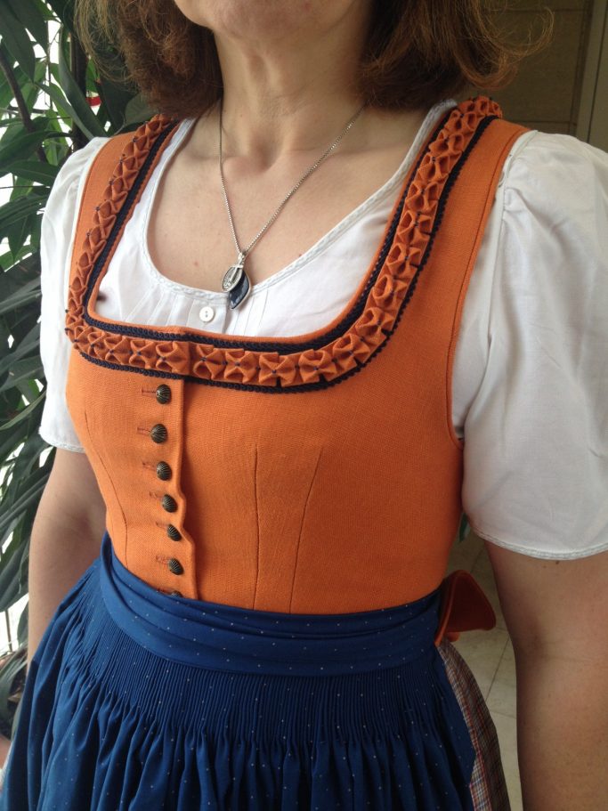 Frau trägt ein traditionelles Dirndl in Orange und Blau mit dekorativem Ausschnitt.