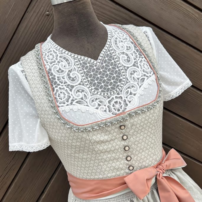 Traditionelles Dirndl in Beige mit Spitzeneinsatz und orangefarbenem Gürtel.