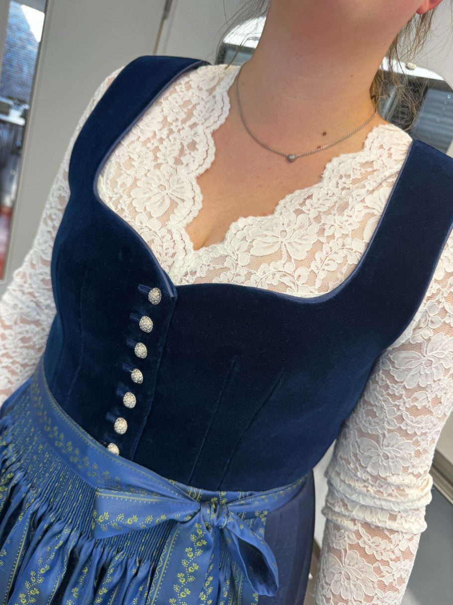 Dunkelblaue Tracht mit Spitzenoberteil und runden Knöpfen, ergänzt durch eine Borte.