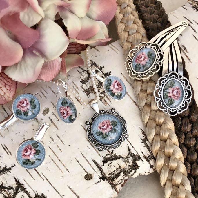 Schmuckset mit rosefarbenen Blumenmotiven auf blauem Hintergrund und silbernen Rahmen.