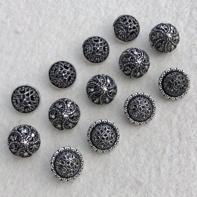 Dunkelgraue, dekorative Knöpfe mit filigranen Mustern und glänzenden Oberflächen.