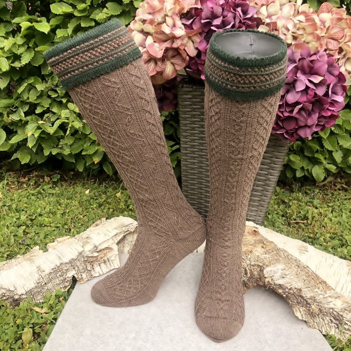 Beige Strümpfe mit grünem Bündchen, auf einem Steinboden mit blühenden Pflanzen im Hintergrund.