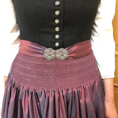 Dirndl mit schwarzem Oberteil, lilafarbener Schürze und silberner Schnalle.