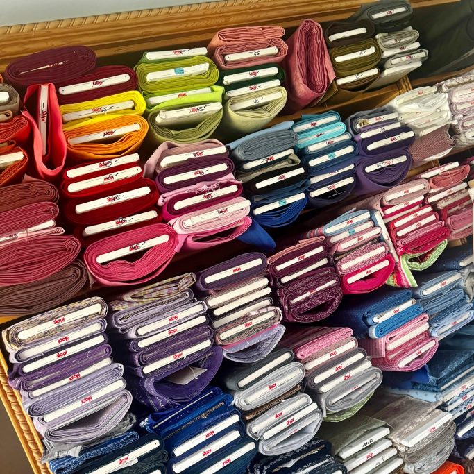 Bunte Stoffrollen in Regalen, sortiert nach Farbe und Größe.