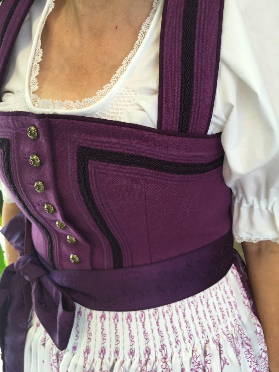 Dirndl in lila mit weißen Rüschen und Schmuckknöpfen, detailreiche Verarbeitung.