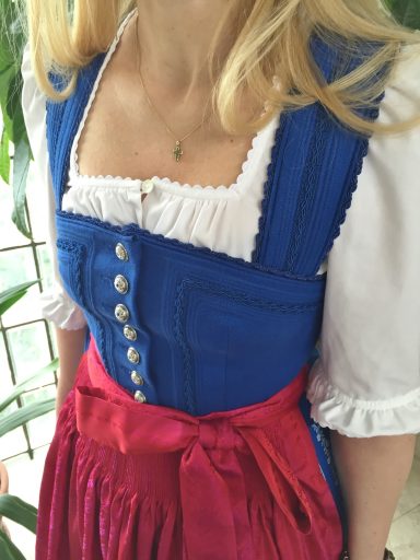 Trachtenkleid mit blauem Mieder und rotem Rock, verziert mit weißen Rüscheln.